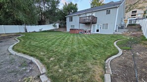 A residential backyard with a well-maintained lawn, a wooden deck, and a white fence. - Feel cozy and at home! Perfect Location For Exploring! (Provo)