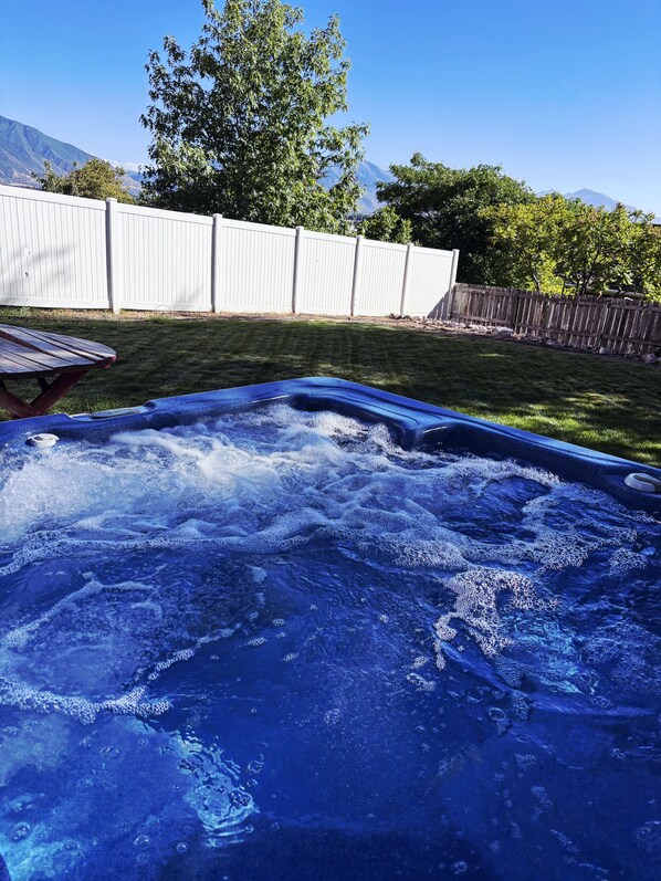 Ein Whirlpool in einem Garten mit Holzzaun und Bäumen im Hintergrund.