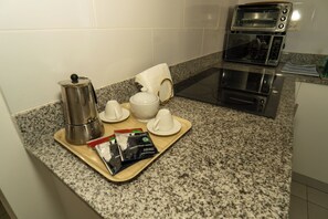 A breakfast tray with a coffee pot, teapot, cups, and a magazine on a granite countertop in a kitchen with a microwave and toaster.