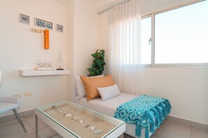 Un salon moderne avec un canapé, une table basse en verre ornée de coquillages, une plante et une fenêtre avec des rideaux.
