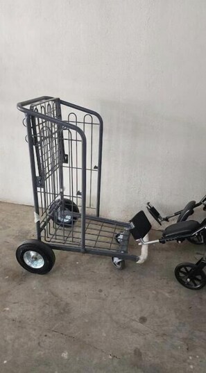 A metal shopping cart with wheels and a handle, placed on a concrete floor against a plain wall. - Comfortable 1BR apt, swimming pool (Playa Juan Dolio)