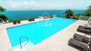 Una piscina con vista sull'oceano, sdraio e una piccola barca.