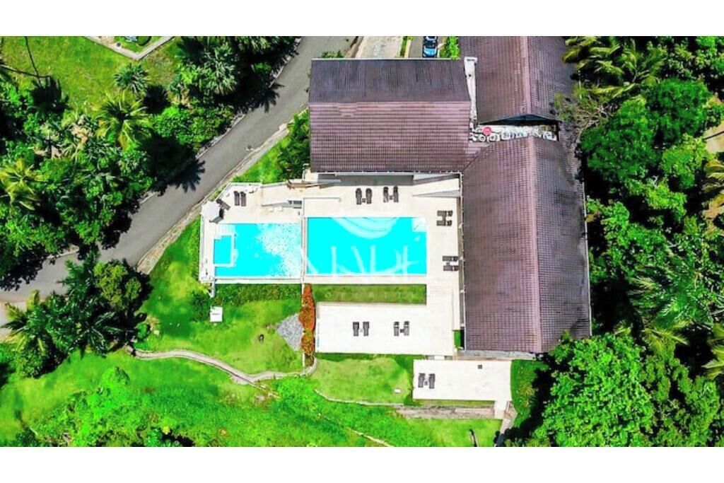 Vista aérea de un edificio con piscina, rodeado de vegetación y una calle pavimentada.