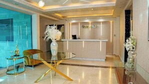 A modern hotel lobby with a reception desk, a glass table with a gold frame, and a vase with white flowers.
