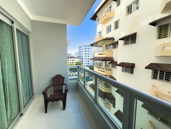 Un balcon avec une chaise, une rambarde en verre et une vue sur les bâtiments voisins.