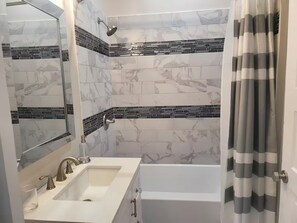 Casa de banho com lavatório branco, espelho, chuveiro com efeito de chuva e banheira.