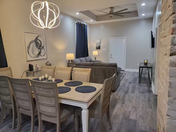 Uma sala de jantar com uma mesa posta para quatro pessoas, um sofá e um ventilador de teto.