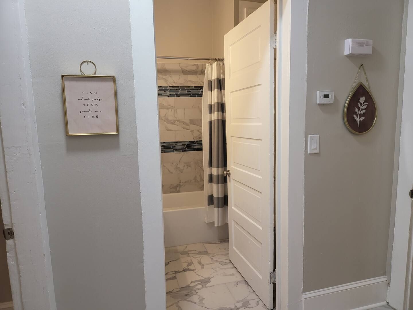 Une salle de bain avec une douche, une citation inspirante encadrée et un thermostat fixé au mur.