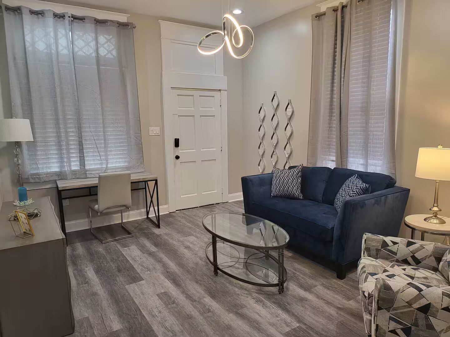 A modern living room with a blue sofa, a glass coffee table, and a patterned armchair.