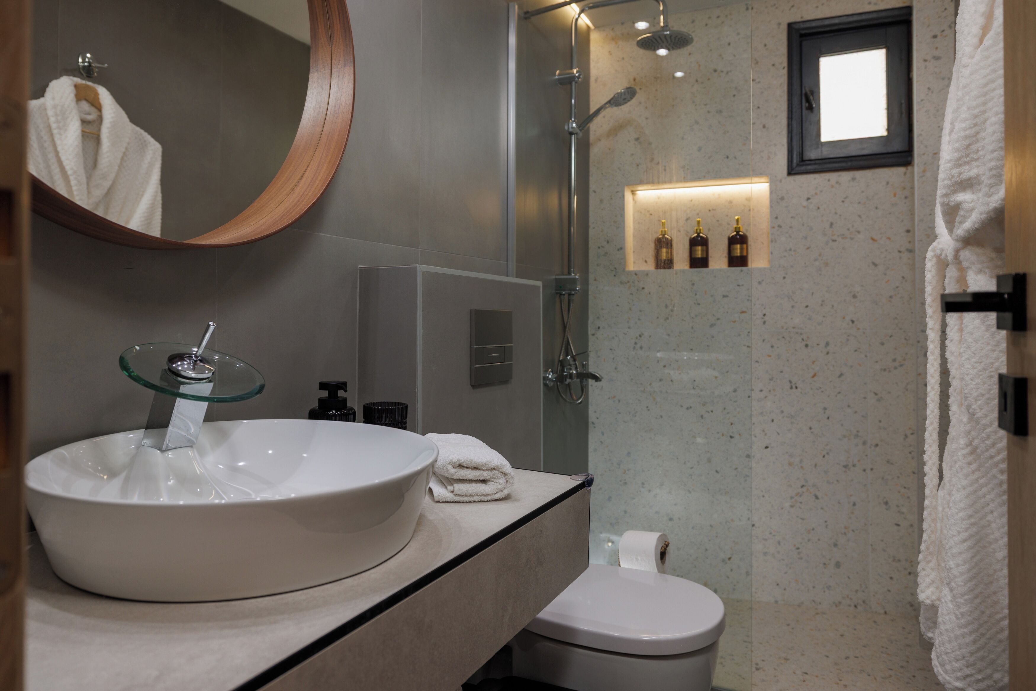 Een badkamer met een groot wit wastafel, een spiegel met glazen rand, een toilet en een douchecabine met glazen wanden.