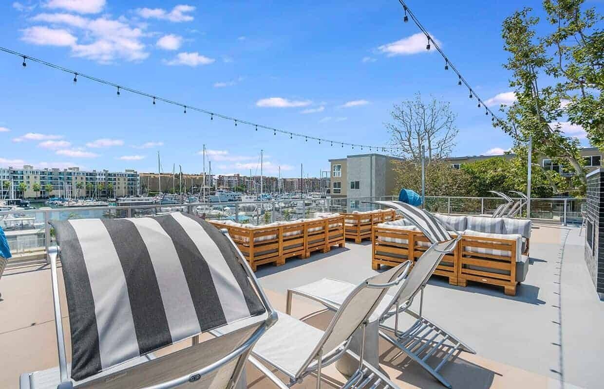 Eine Dachterrasse mit Liegestühlen und einem gestreiften Sonnenschirm mit Blick auf einen Hafen voller Boote und Gebäude.