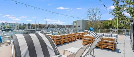 Eine Dachterrasse mit Liegestühlen und einem gestreiften Sonnenschirm mit Blick auf einen Hafen voller Boote und Gebäude.