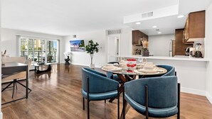 A modern kitchen with wooden cabinets, a dining area with blue chairs, and a large window offering a city view. - The Mahogany' Full Boats View Marina Front Row Dream Pool, Jacuzzi And Gym (Marina del rey)