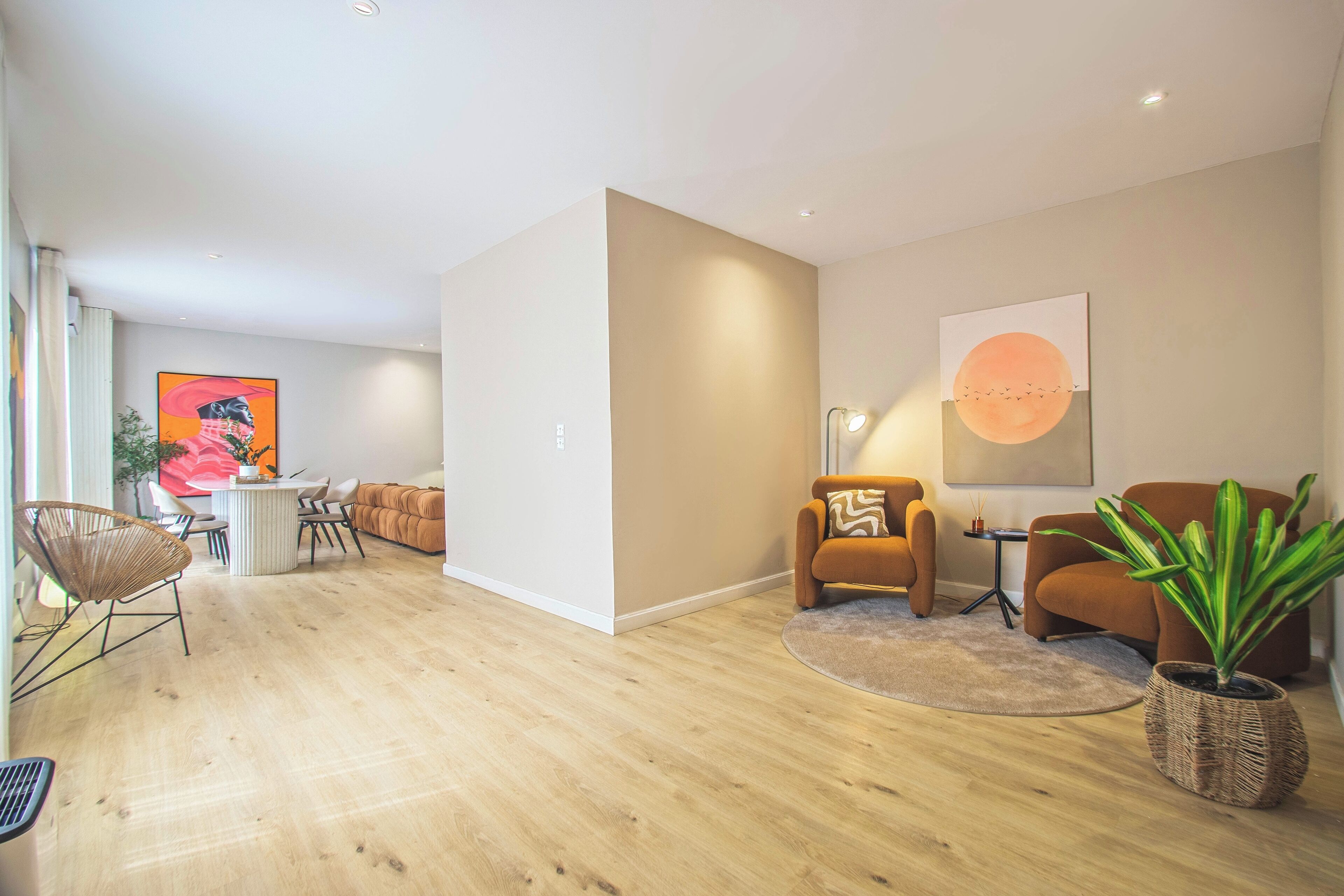A modern living room with a wooden floor, a round coffee table, a sofa, a chair, and a potted plant.