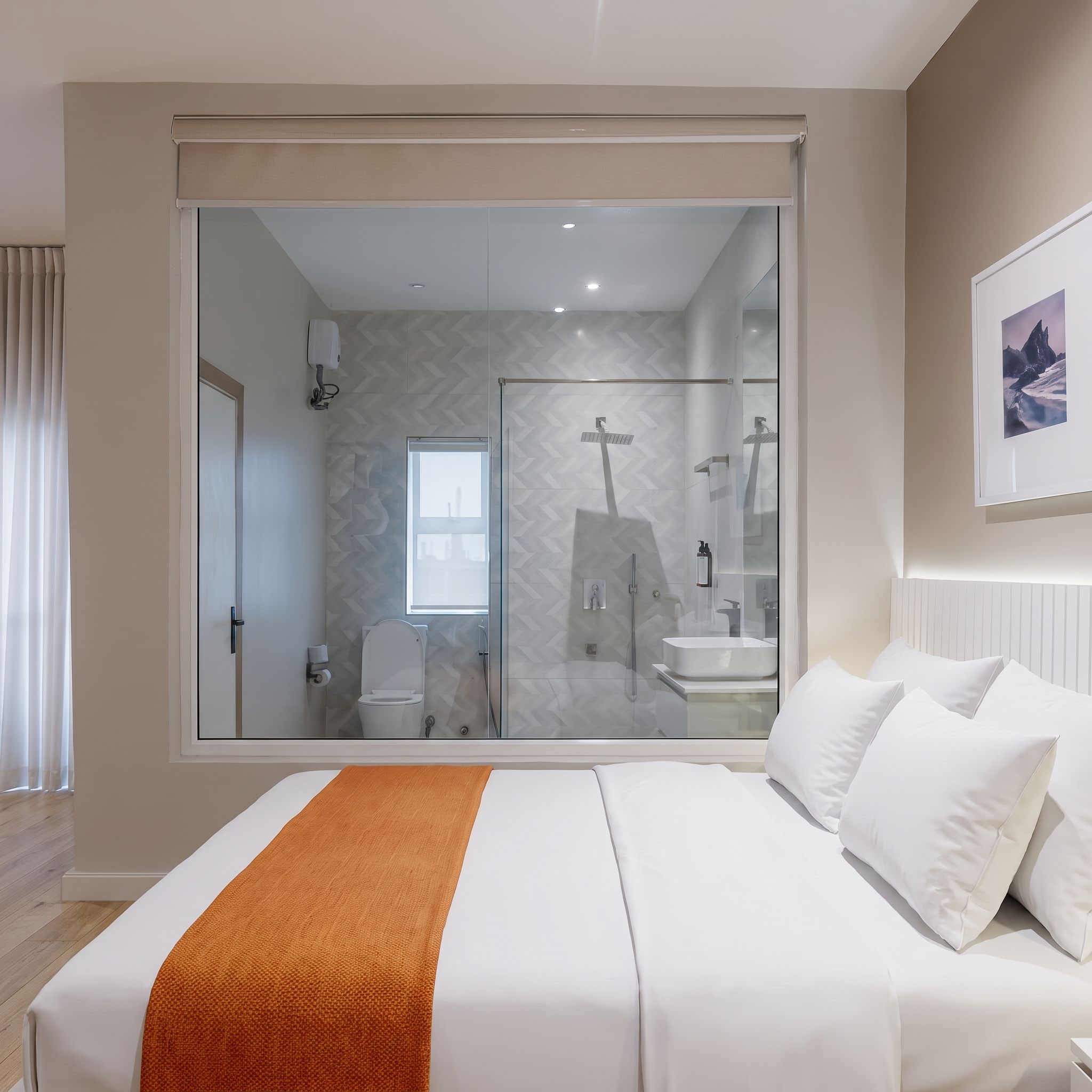 A modern bedroom with a large bed, a sliding glass door to a bathroom, and a framed picture on the wall.