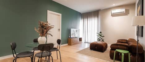 A modern living room with a glass dining table, dark chairs, a brown sofa, and a green stool.