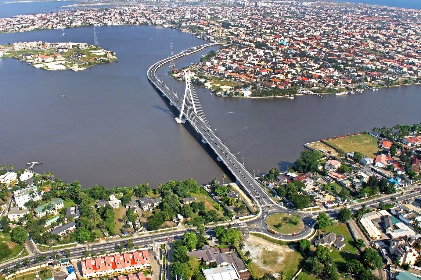 An aerial view of a city with a prominent bridge spanning a river, surrounded by residential areas and greenery.