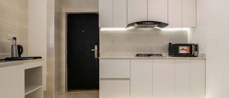 A modern kitchen with white cabinetry, a black door, and a Kenwood microwave on the counter.