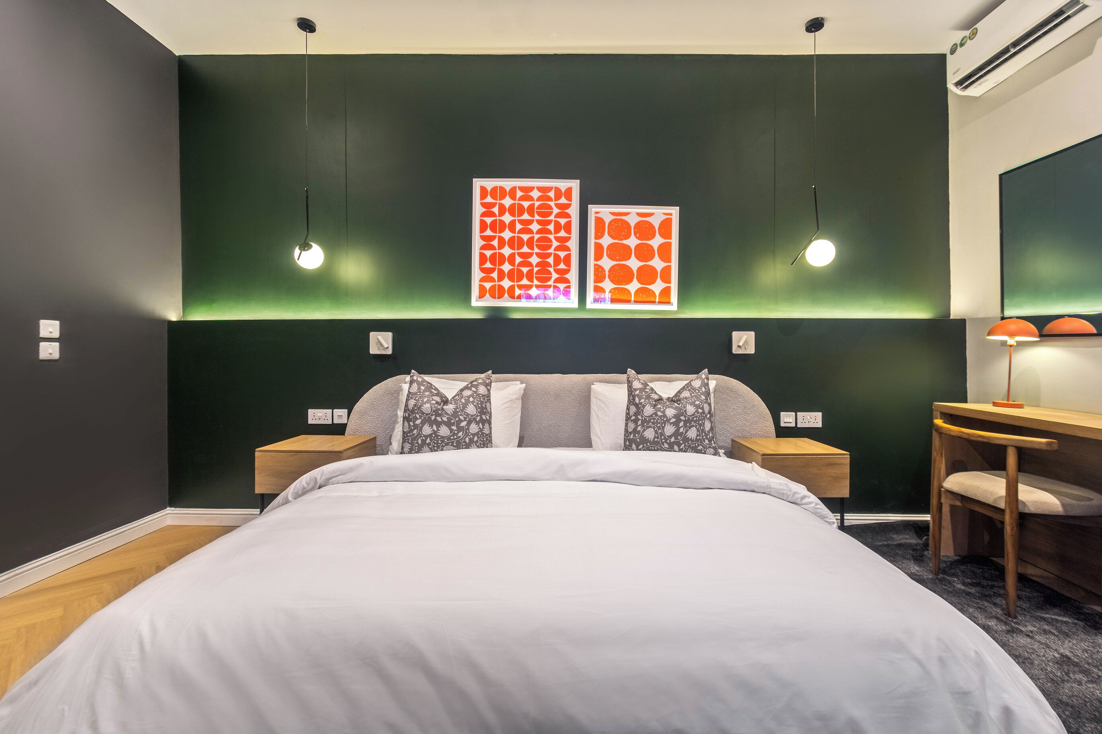 A modern bedroom with a large bed, two bedside tables, a desk with a chair, and two wall-mounted light fixtures.