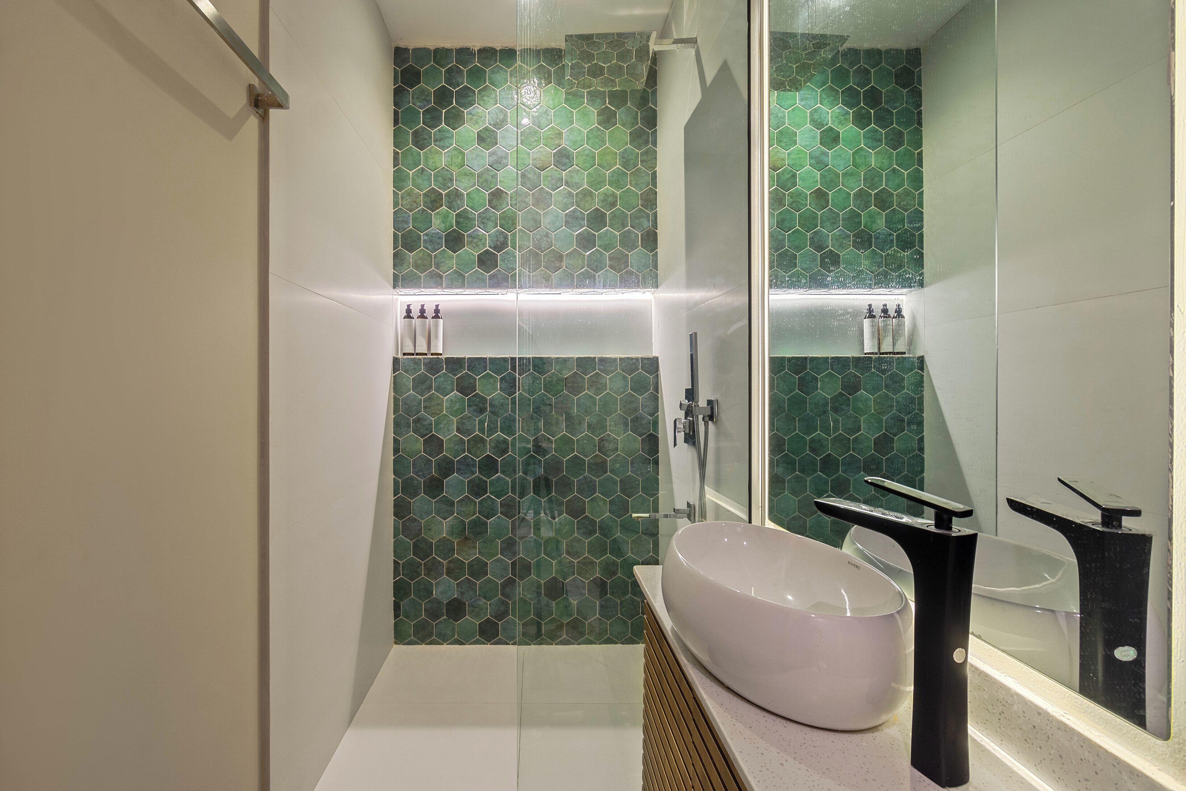 Un bagno moderno con cabina doccia in vetro, lavandino bianco e parete rivestita in mosaico verde.