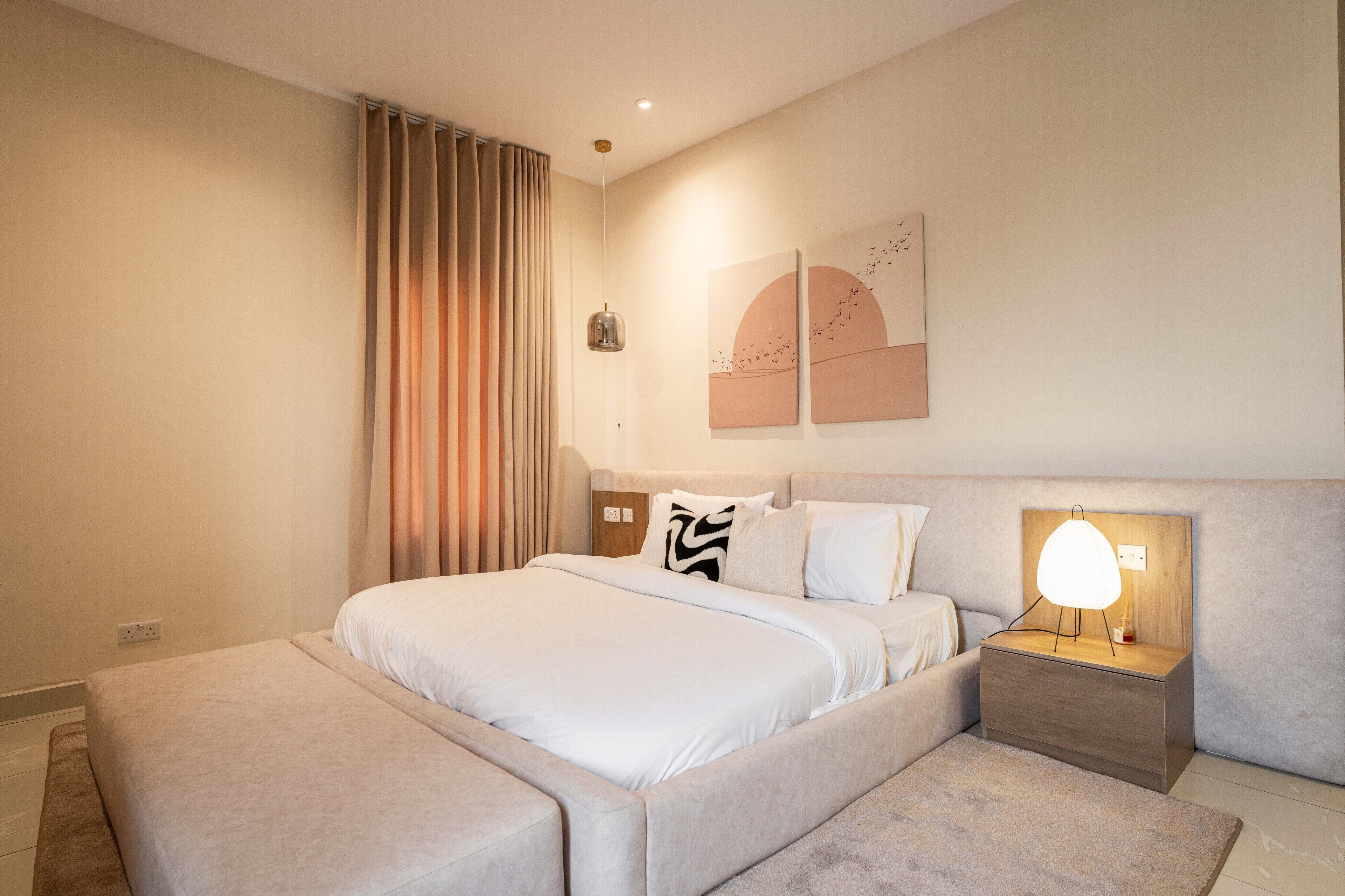 A modern bedroom with a large bed, a bedside table with a lamp, and abstract wall art.