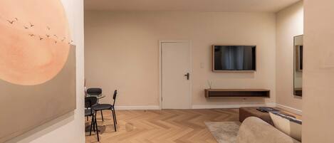 Una sala de estar moderna con suelo de parqué de espiga, un sofá, un televisor montado en la pared y una puerta que da a otra habitación.