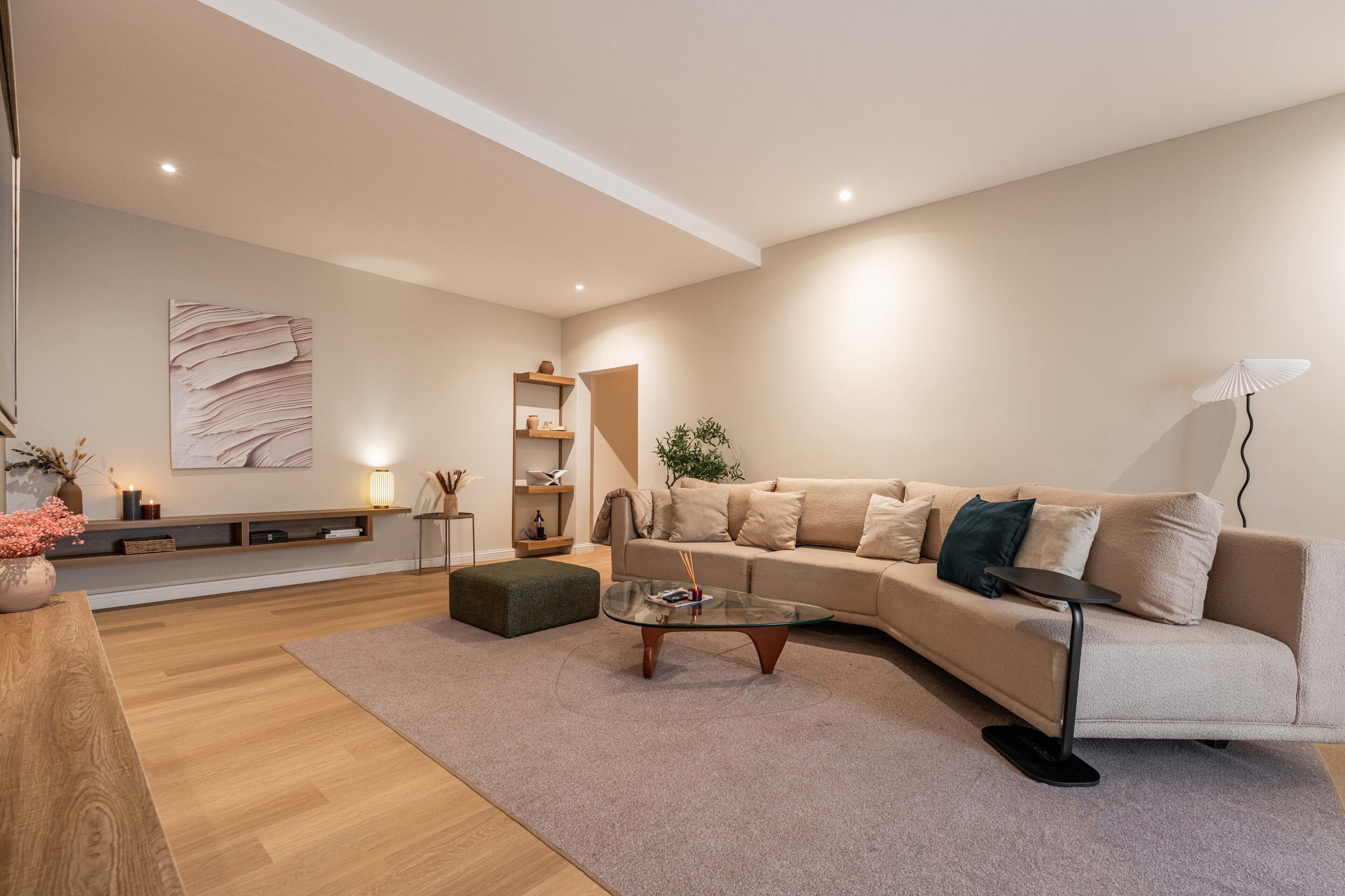 A modern living room with a beige sofa, a glass coffee table, a wooden side table, and a minimalist decor.