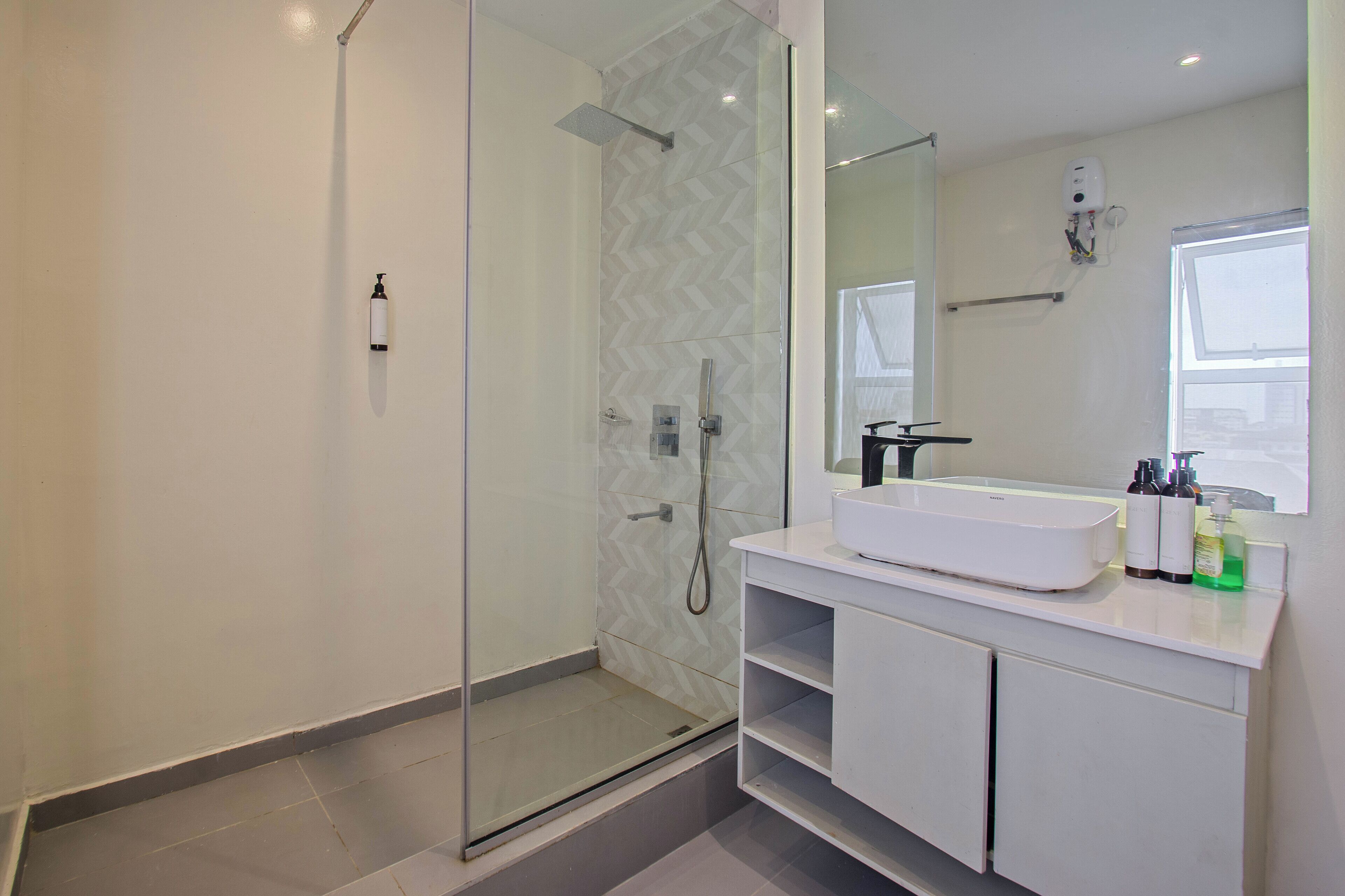 Un baño moderno con ducha compartimentada por vidrio, un lavamanos blanco y un espejo grande.