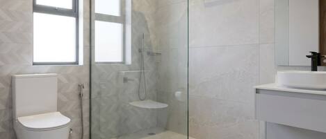 Un baño moderno con ducha de vidrio, inodoro y lavamanos con espejo arriba.