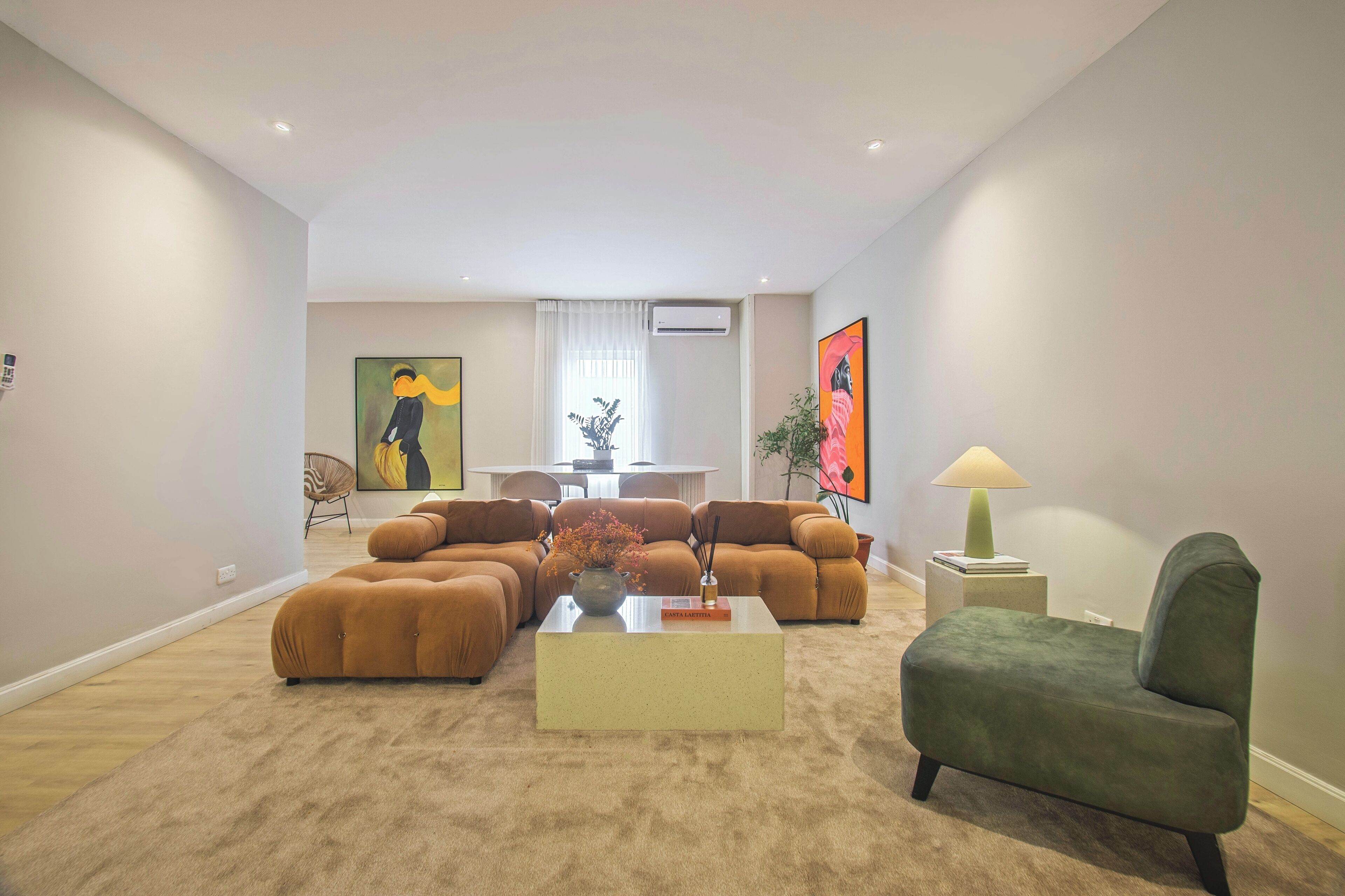 Un salon moderne avec un canapé d’angle, un fauteuil vert et une table basse. On aperçoit à l’arrière-plan un coin repas avec une table et des chaises.