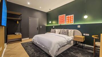Quarto moderno com cama grande, mesa de cabeceira, guarda-roupa e televisão.