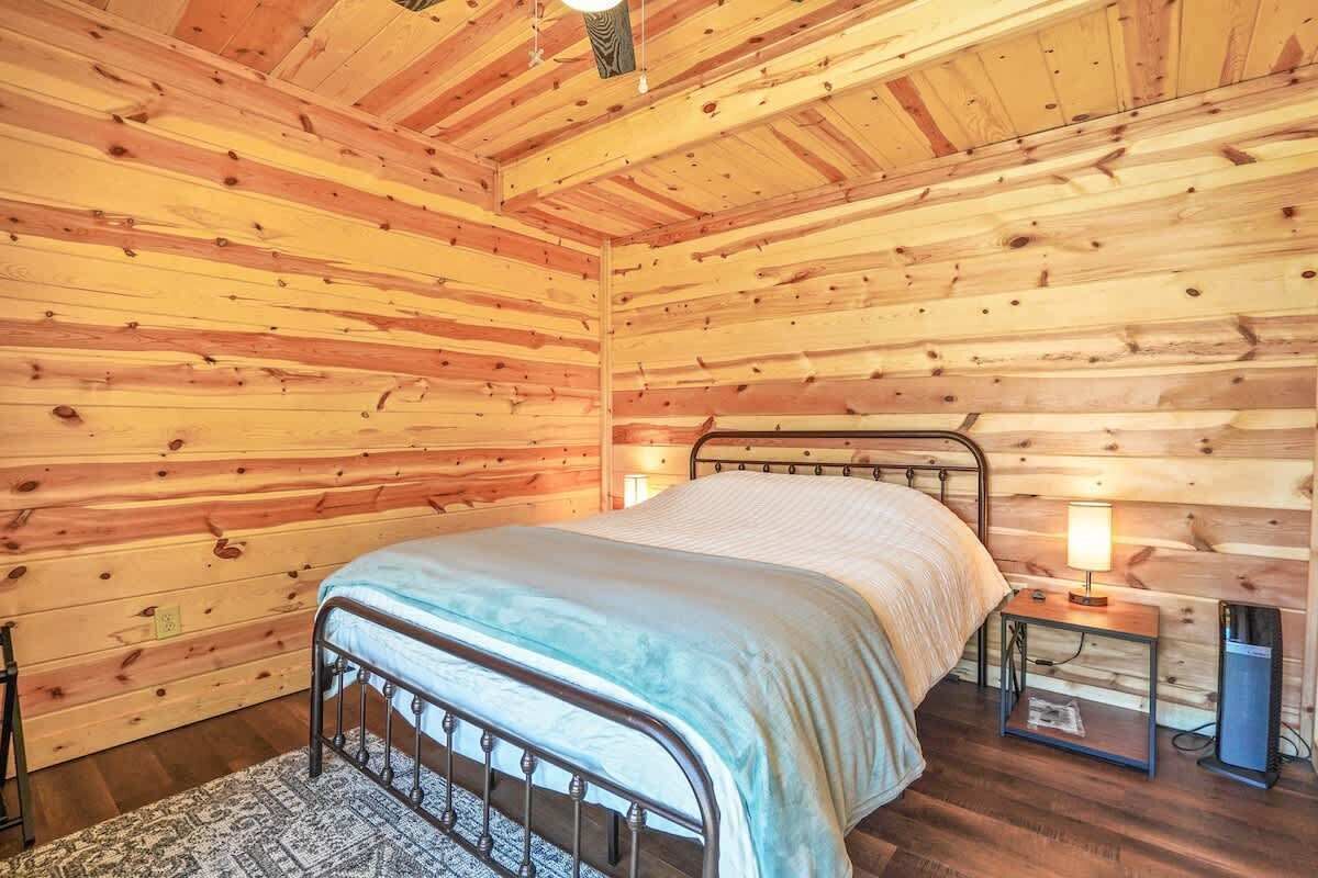 A wooden cabin bedroom with a metal bed frame, a bedside table with a lamp, and a small nightstand.
