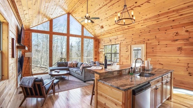 A spacious cabin with a large living area, a kitchen with a central island, and large windows offering views of the surrounding forest. - Fern Woods A Modern Take on Hocking Hills Cabins (McArthur)