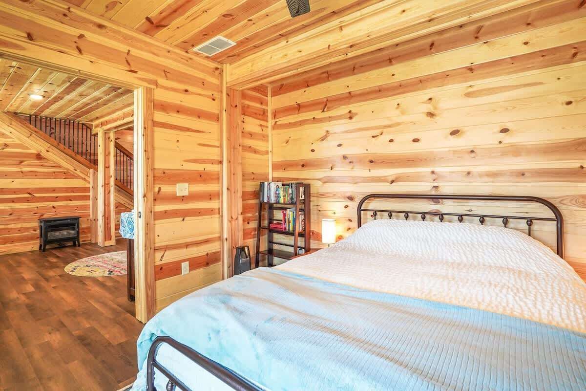 Un dormitorio de cabaña de madera con una cama, una estantería y una escalera que lleva a un nivel superior.