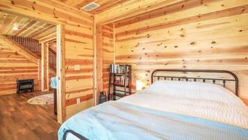 Un dormitorio de cabaña de madera con una cama, una estantería y una escalera que lleva a un nivel superior.