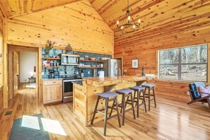 A wooden cabin interior with a kitchen, bar stools, and a large window. - Fern Woods A Modern Take on Hocking Hills Cabins (McArthur)