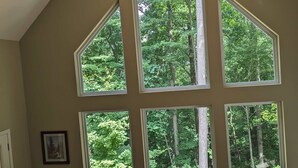 Una habitación amplia con techo alto y ventanas grandes que dan a un bosque.
