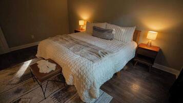 Un dormitorio con una cama grande, dos lámparas de noche, una alfombra y un taburete pequeño.