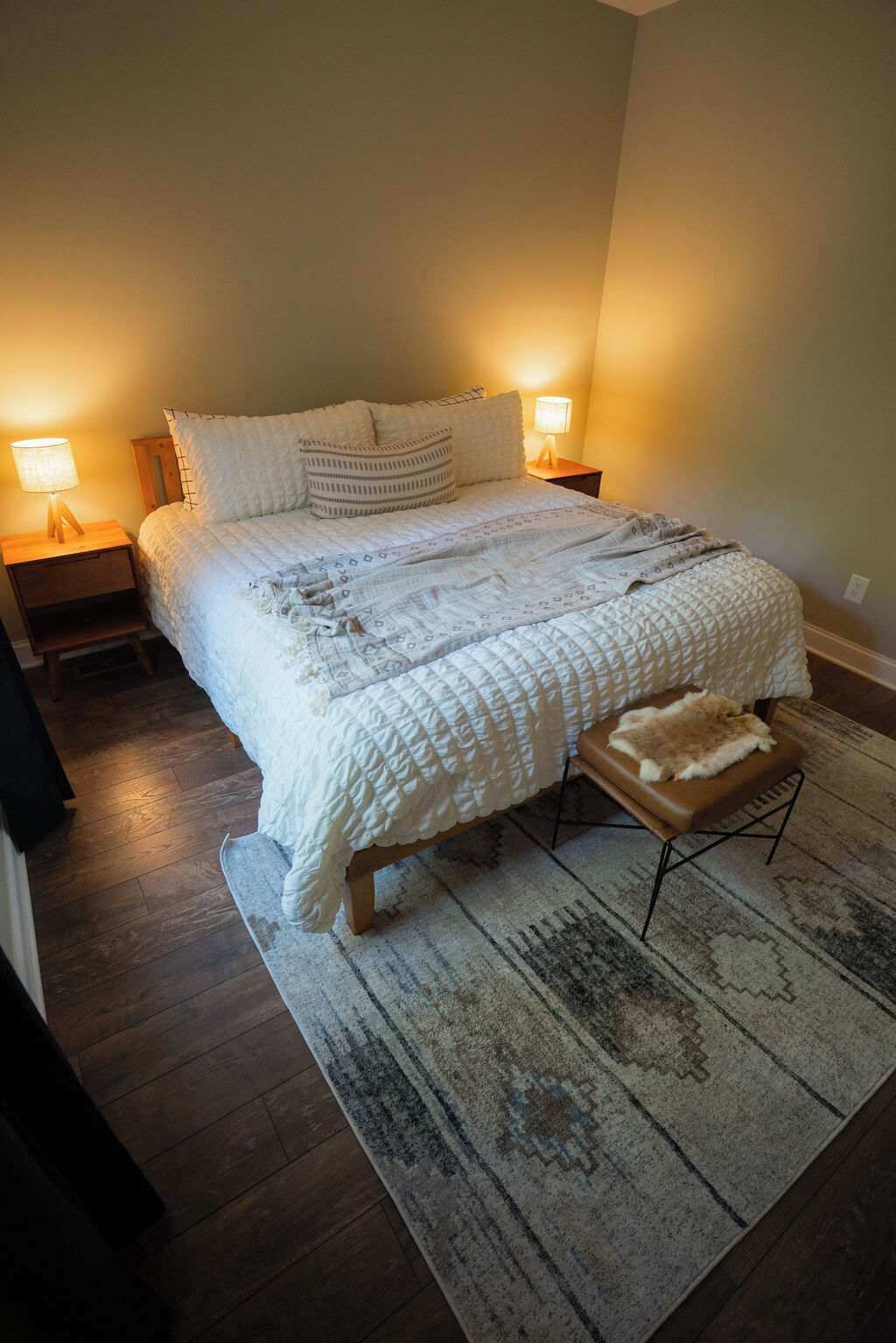Ein Schlafzimmer mit einem großen Bett, zwei Nachttischlampen, einer Bank und einem gemusterten Teppich.