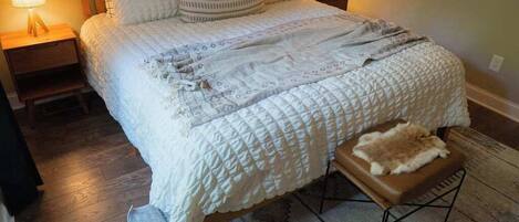 A bedroom with a large bed, two bedside lamps, a bench, and a patterned rug.