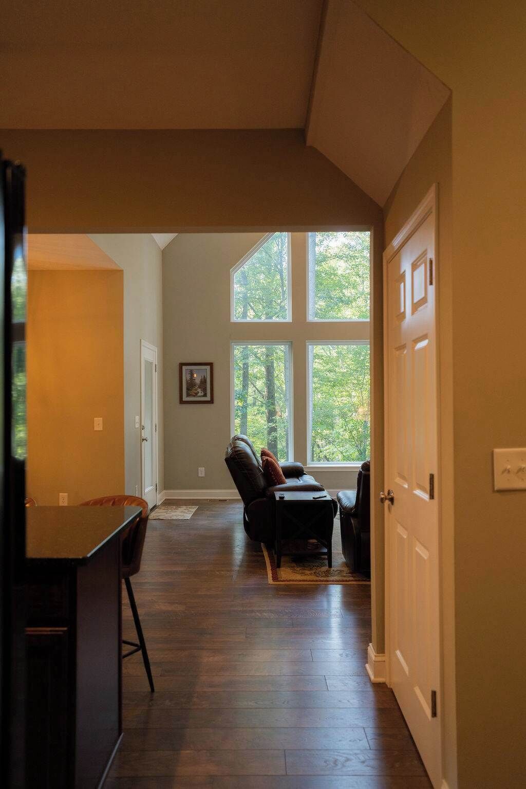 A spacious room with a large window, a dark wooden floor, and a leather recliner.