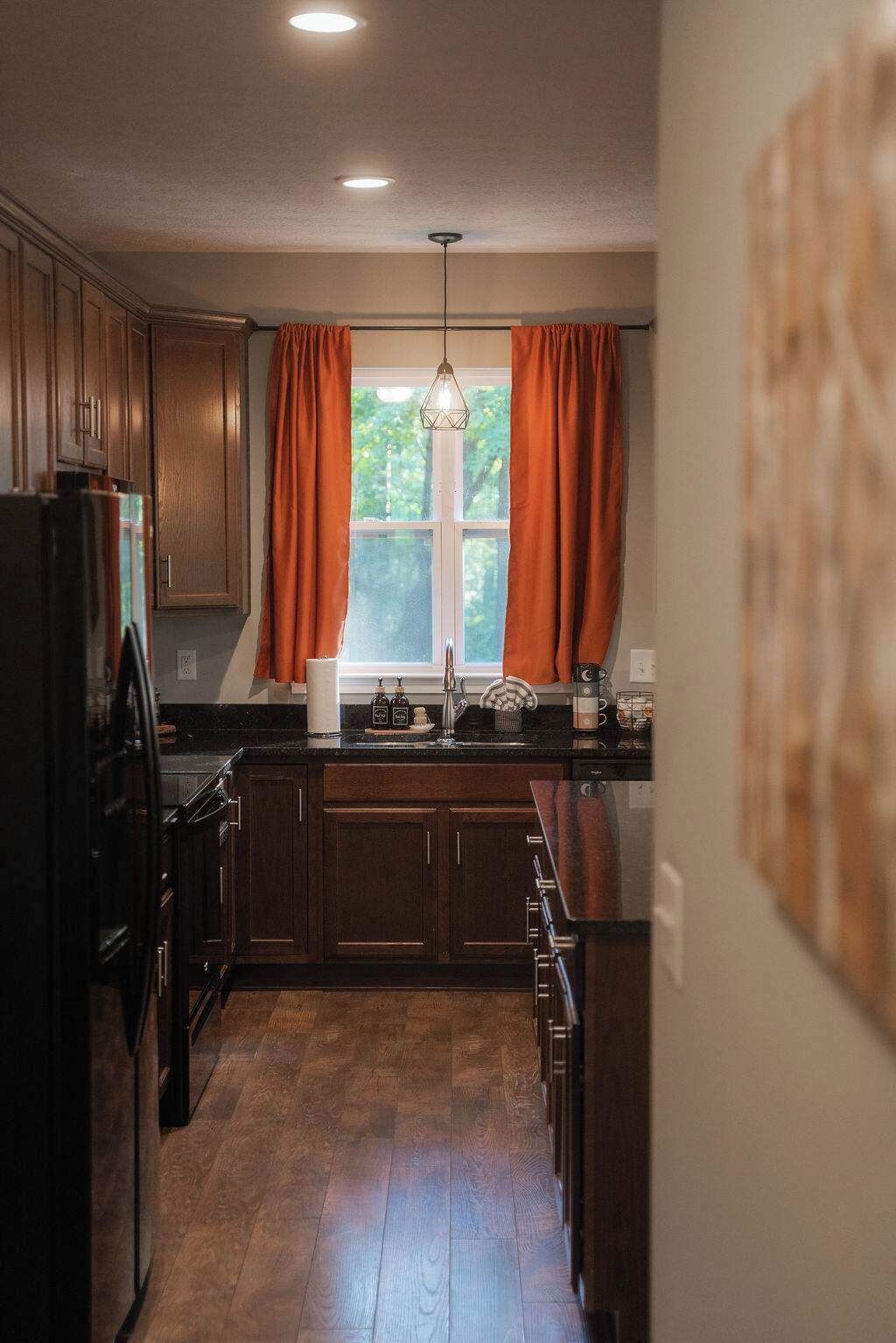 A kitchen with wooden cabinets, a window with orange curtains, and a hanging light fixture.