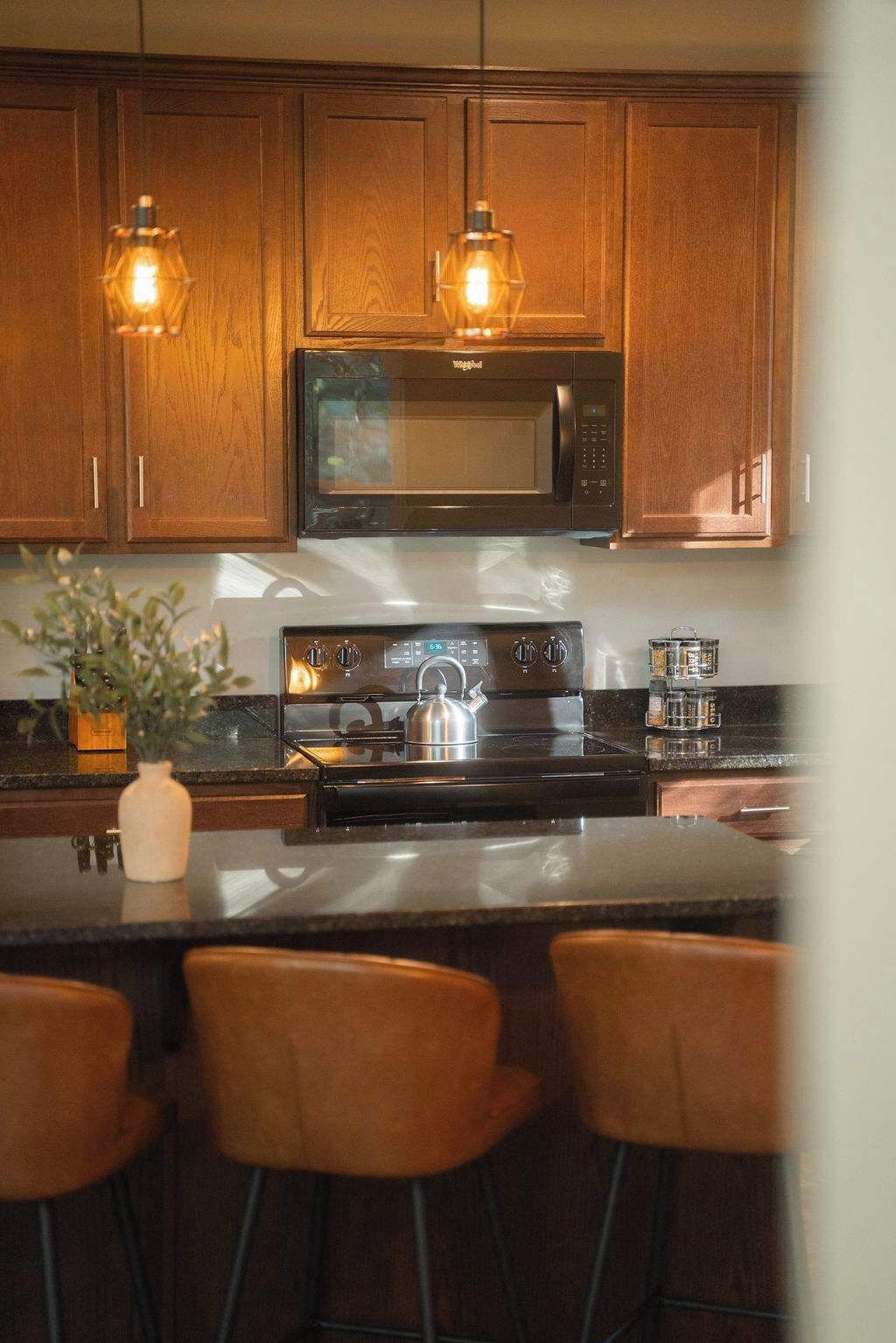 A kitchen with wooden cabinets, a microwave, a stove, and a bar area with stools.