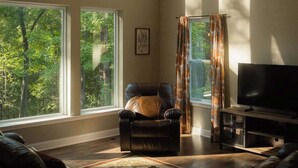 Un salón amplio con ventanas grandes, un sillón de cuero, un televisor de pantalla plana y una mesa de centro de madera.