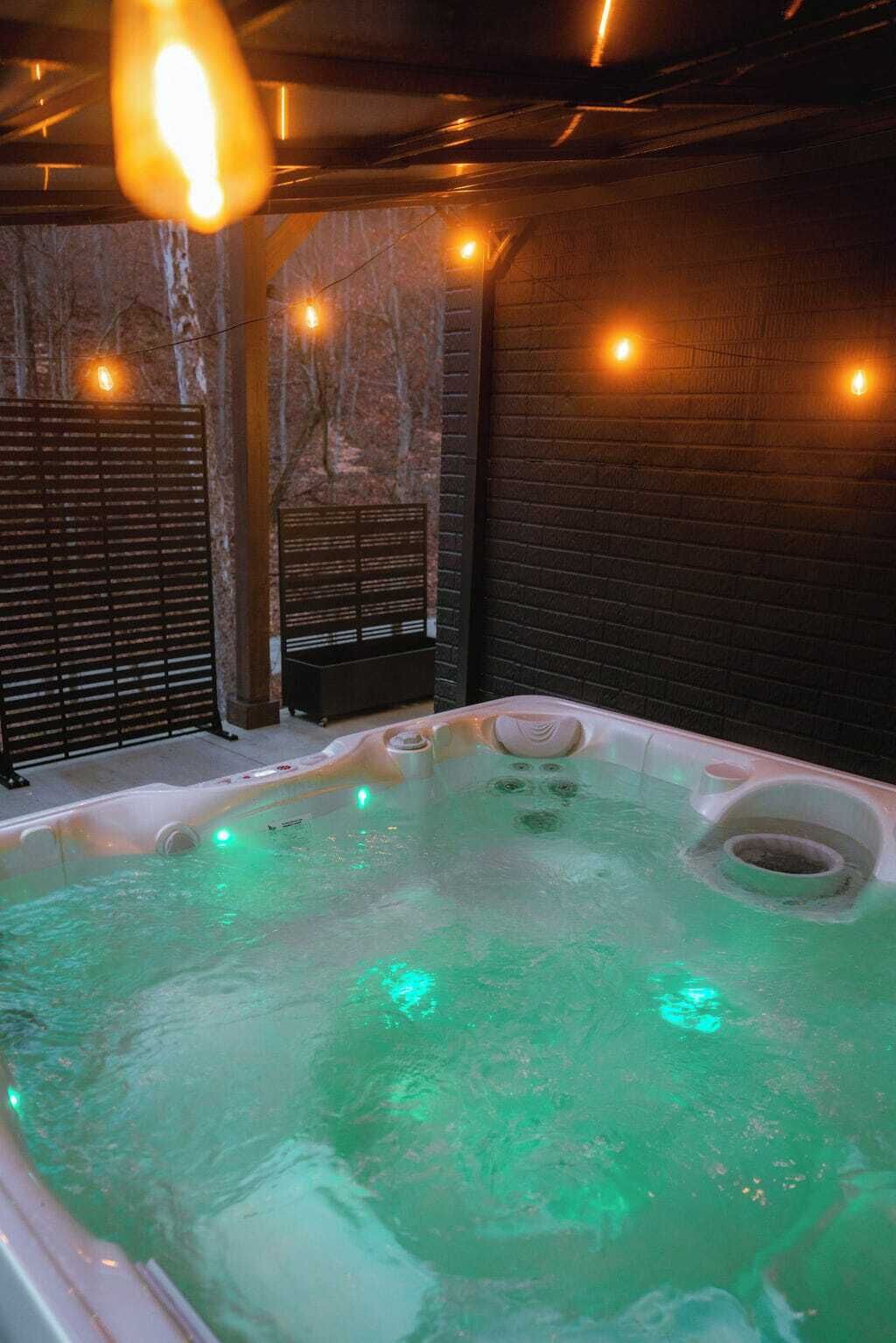 Un jacuzzi iluminado con luz verde, rodeado de paredes de ladrillo y un banco de madera.