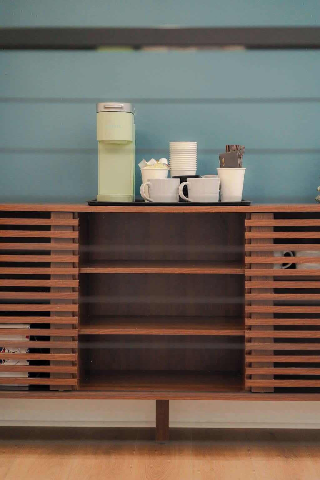 Eine Küchenzeile mit Kaffeemaschine, gestapelten weißen Tassen und einem kleinen Schrank.