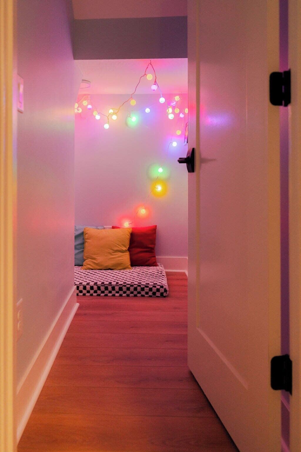 Ein schmaler Flur mit einem Bett am Ende, dekoriert mit bunten Lichterketten.