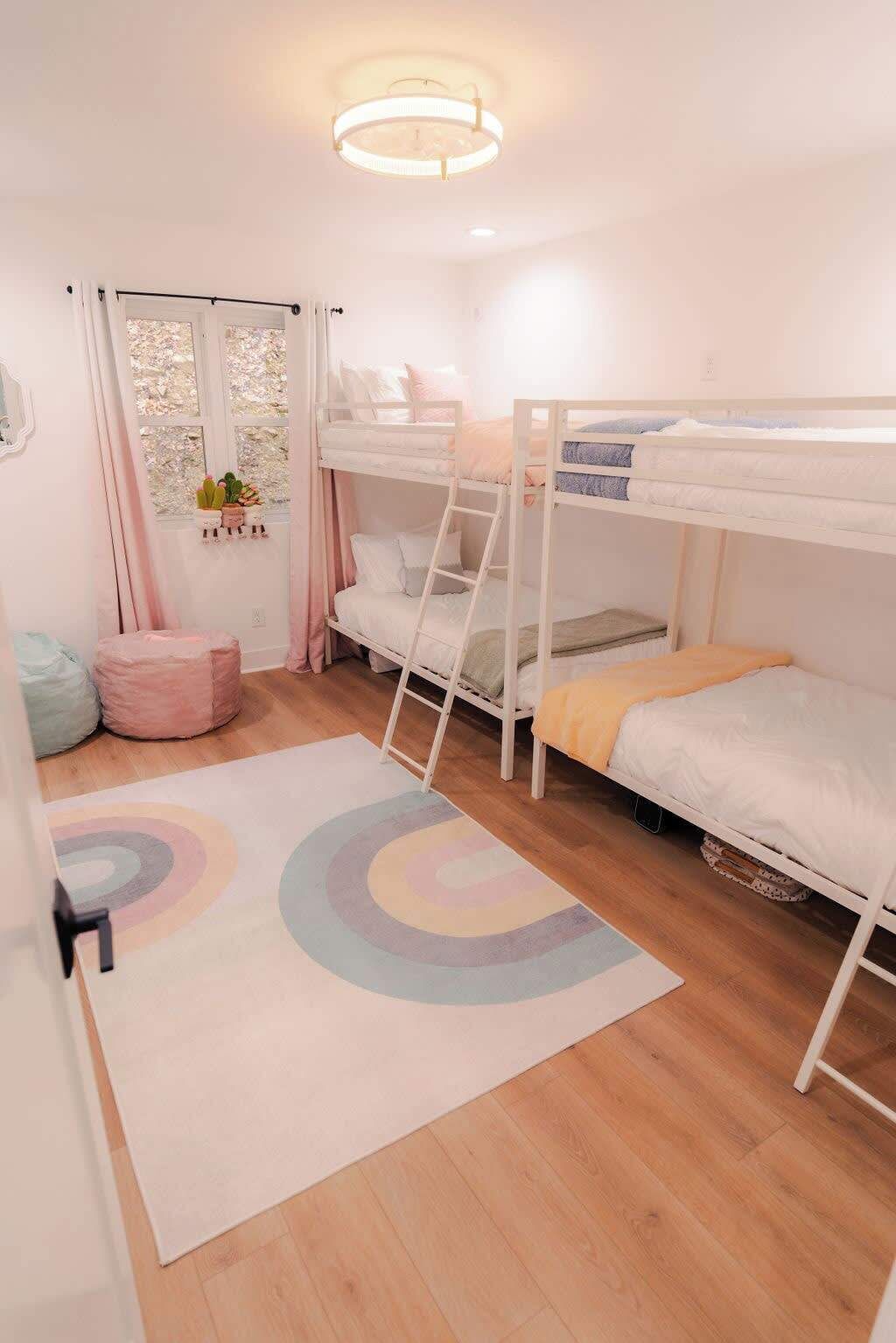 Une chambre avec des lits superposés, une petite fenêtre avec des rideaux, une table de chevet et un tapis coloré.