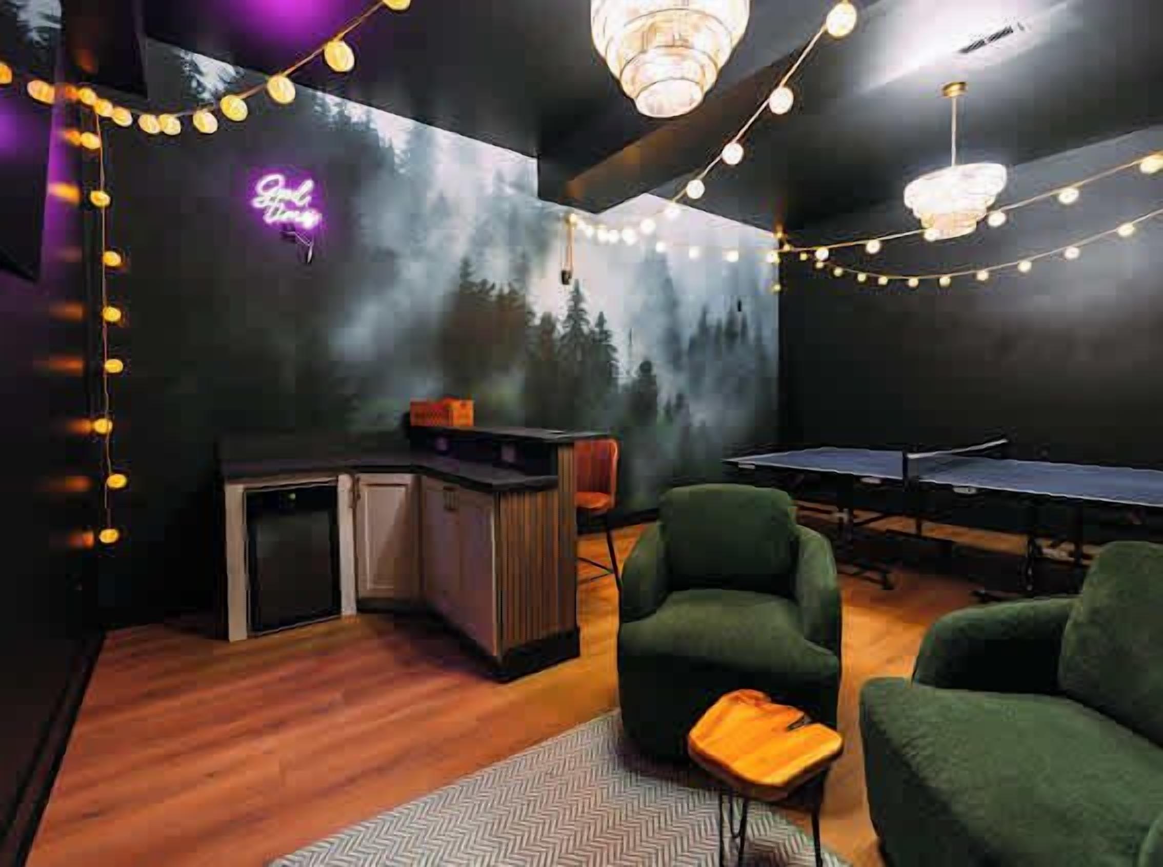 Una habitación con mesa de ping pong, sillones verdes, un letrero de neón y guirnaldas de luces.