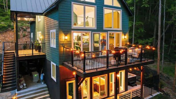 Une cabane à deux étages dotée d’un balcon, de grandes fenêtres et d’une terrasse.